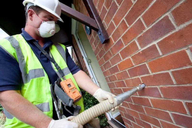 Cavity wall insulation installer wearing PPE pumping material into cavity wall